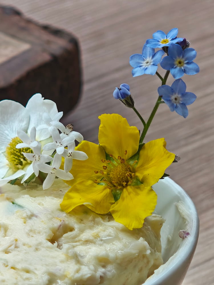 Wildkräuterbutter mit essbaren Blüten auf der Oberfläche