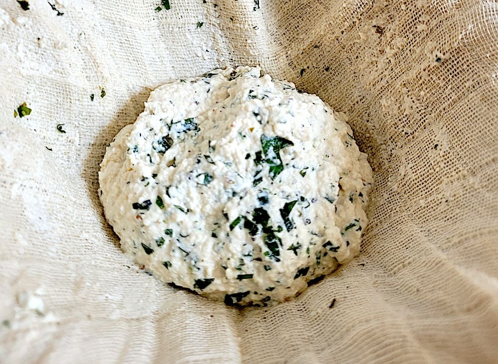 Mit Wildkräutern vermischter Frischkäse in einem Mulltuch Mit Wildkräutern vermischter Frischkäse in einem Mulltuch