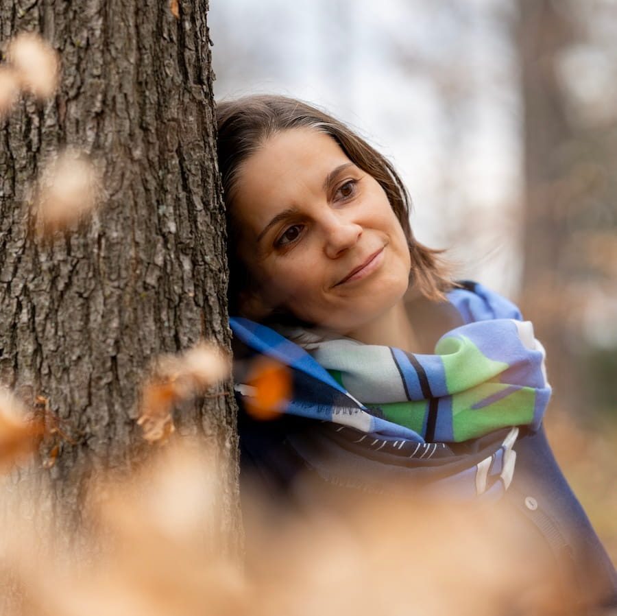 Kräuterpädagogin Rosi Wokurek lehnt an einem Baumstamm im herbstlichen Wald