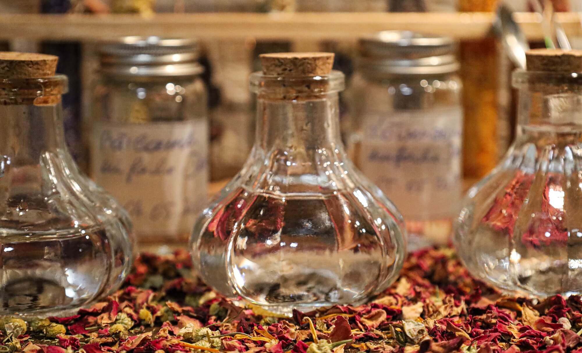 Glasflaschen mit Pflanzenwässern auf getrockneten Rosenblüten – Workshop Hydrolate und ätherische Öle